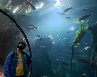 Yuri stands in the underwater tunnel in front of a pretty backdrop of sealife, smiling under his mask