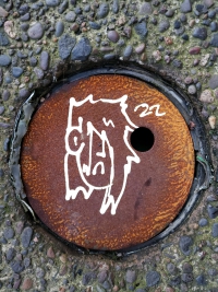 Tag of an emo person with the numbers 22 on a rusted metal manhole cover in a worn-down sidewalk