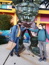 Yuri and Cel jokingly touching the bulge of a giant metal statue of the Hulk. Yuri is laughing, and Cel looks mischevious